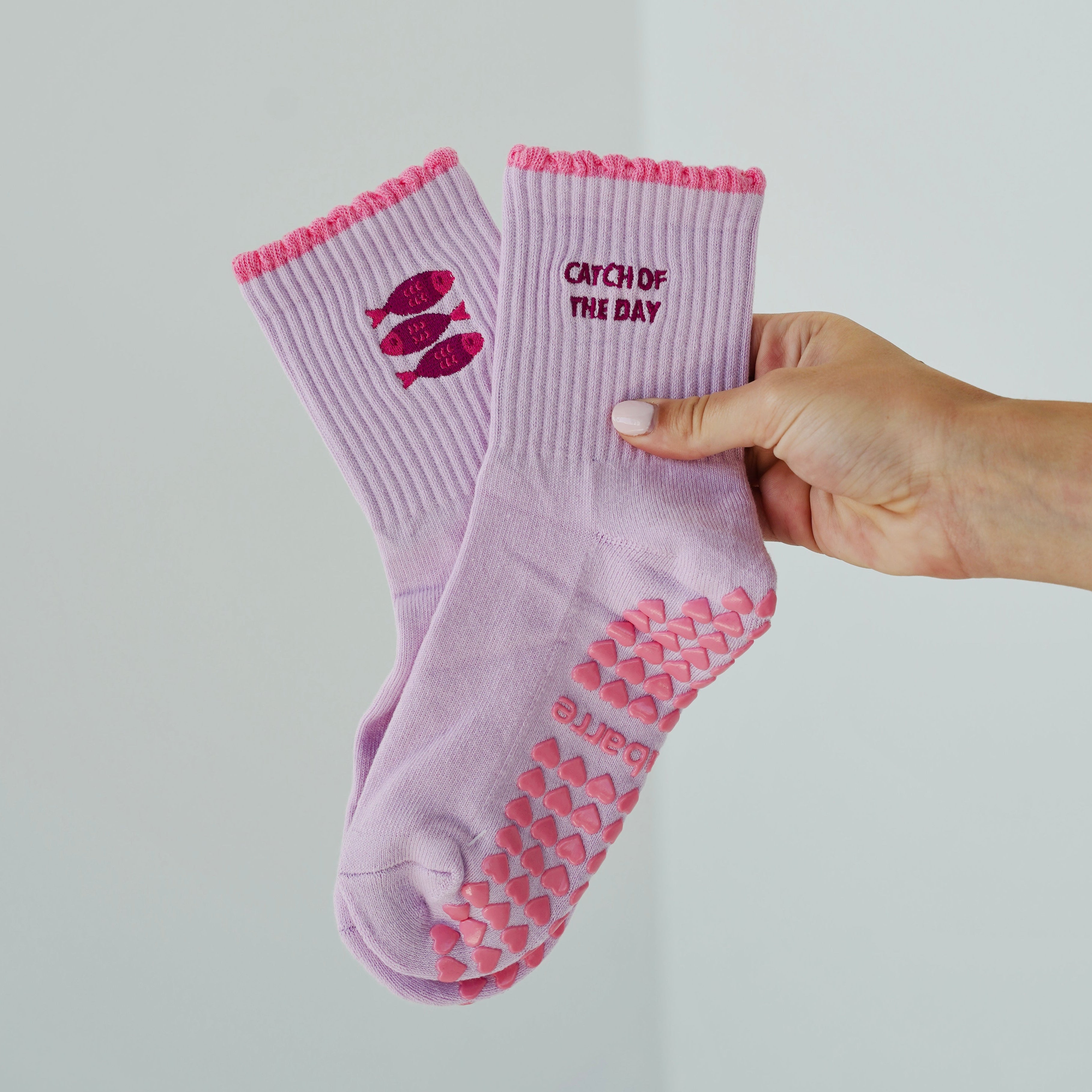 A pair of light purple grip socks and text reading 'CATCH OF THE DAY' on the side with sardines on the other side. Sardine pilates socks