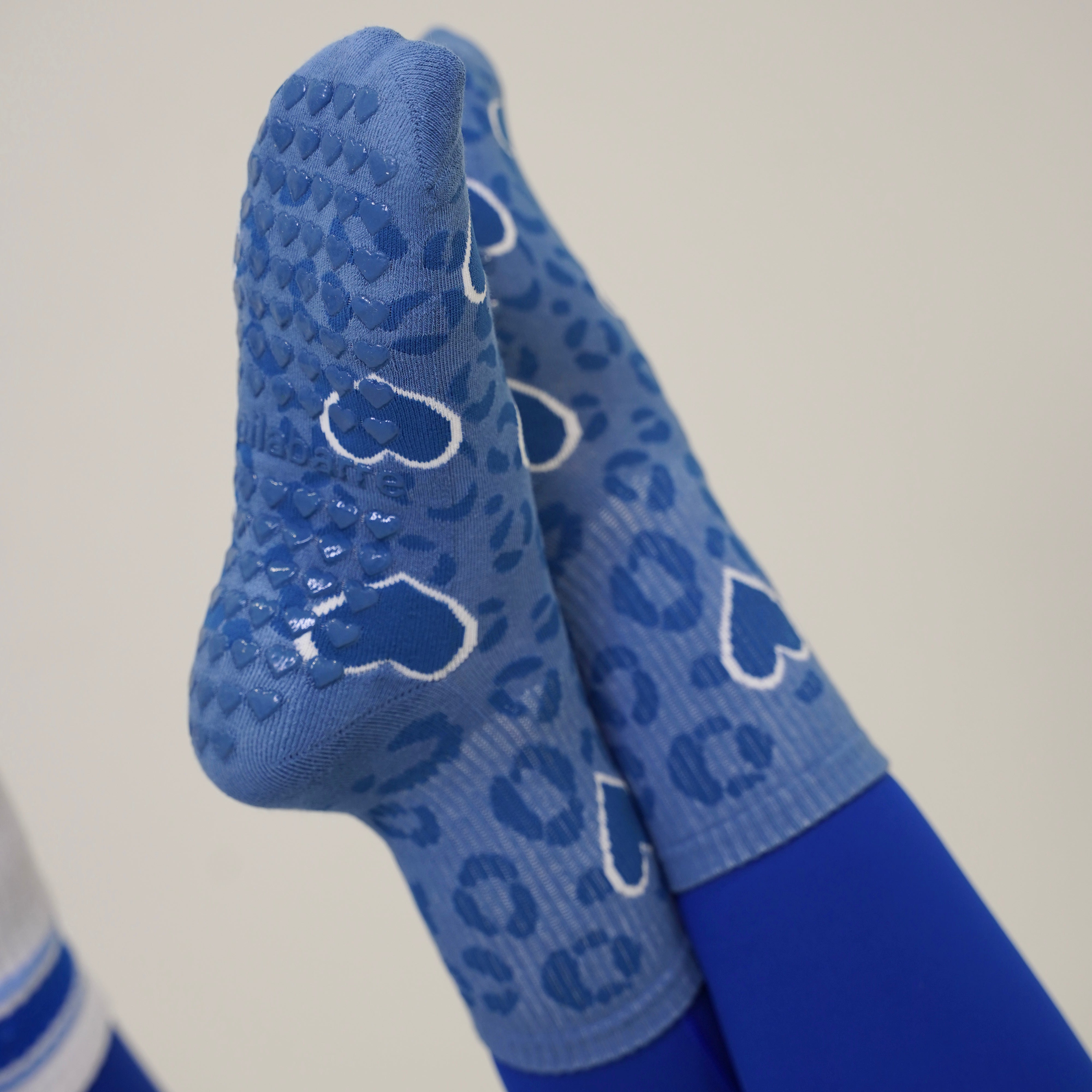 Blue grip socks with a leopard print pattern and white heart outlines, worn on feet with blue leggings against a plain light background. Cheetah Grip socks in blue with hearts