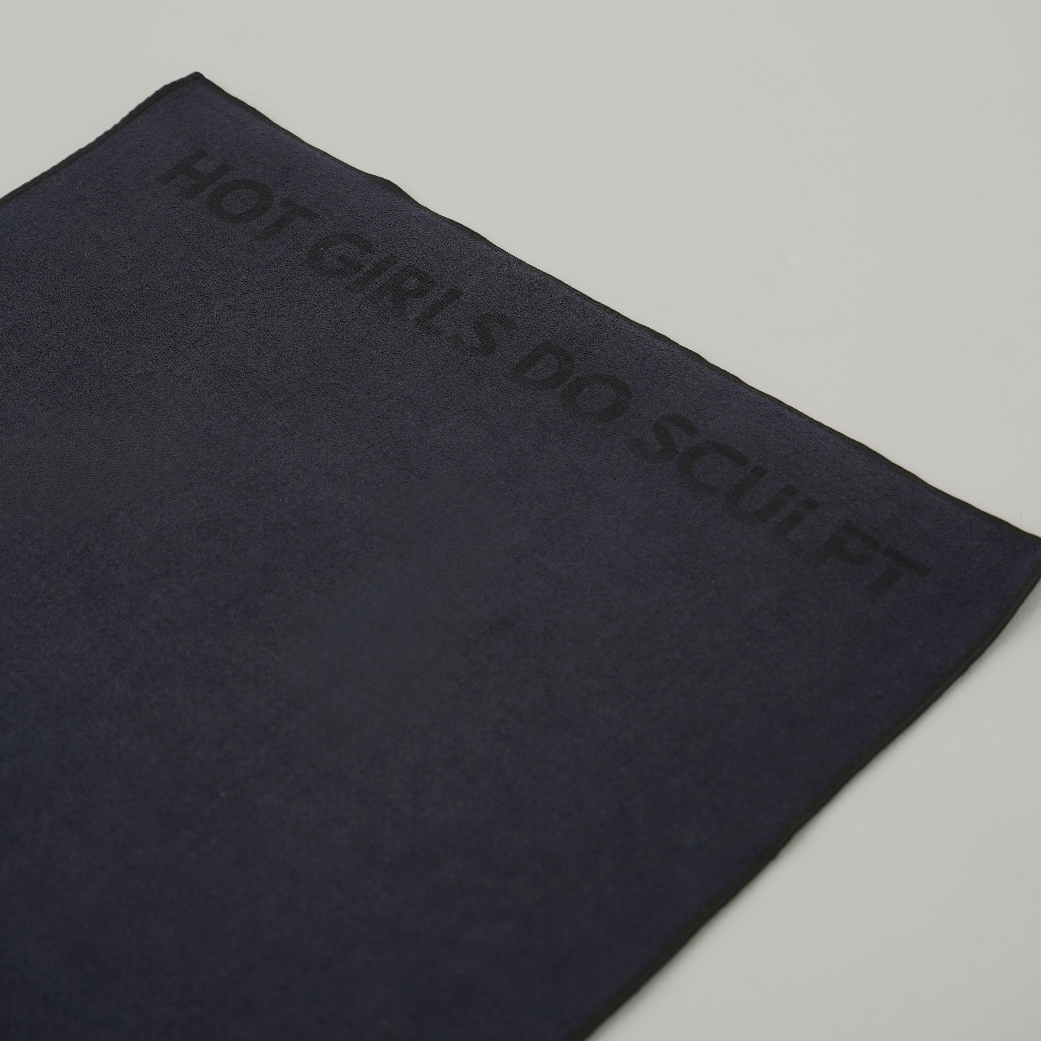 A close-up of a dark grey grip towel or yoga towel featuring the text 'HOT GIRLS DO SCULPT' printed in a matching dark tone on the corner, set against a plain light gray background.