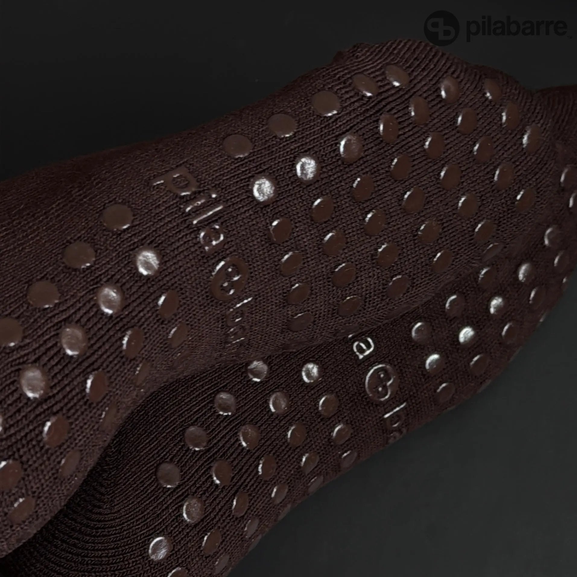 Close-up of a brown Barre Grip Sock with textured surface and pilabarre branding on a dark background