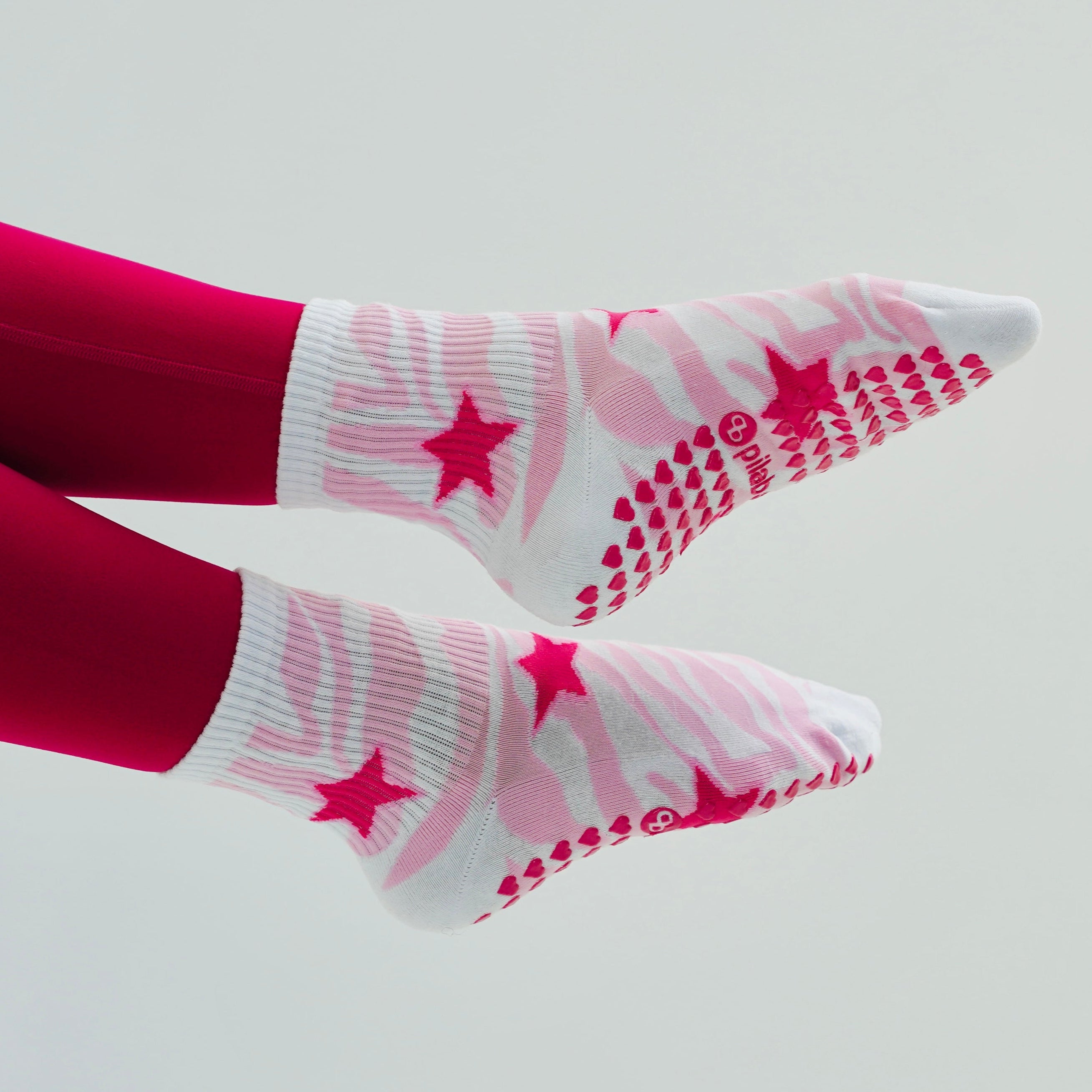 Pink zebra grip socks with pink star and dotted traction patterns, worn with bright pink leggings, shown against a plain light gray background.