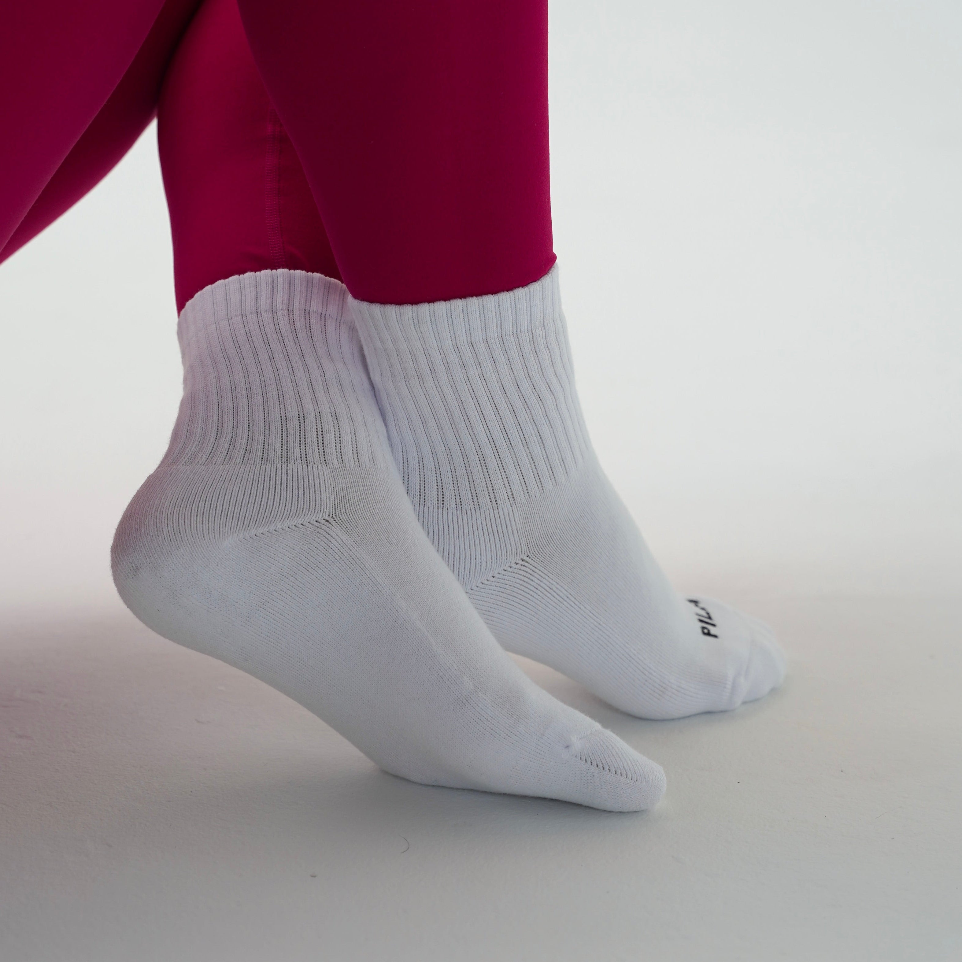 White ribbed crew socks worn on a person's feet, paired with bright magenta leggings, against a clean light gray studio background.