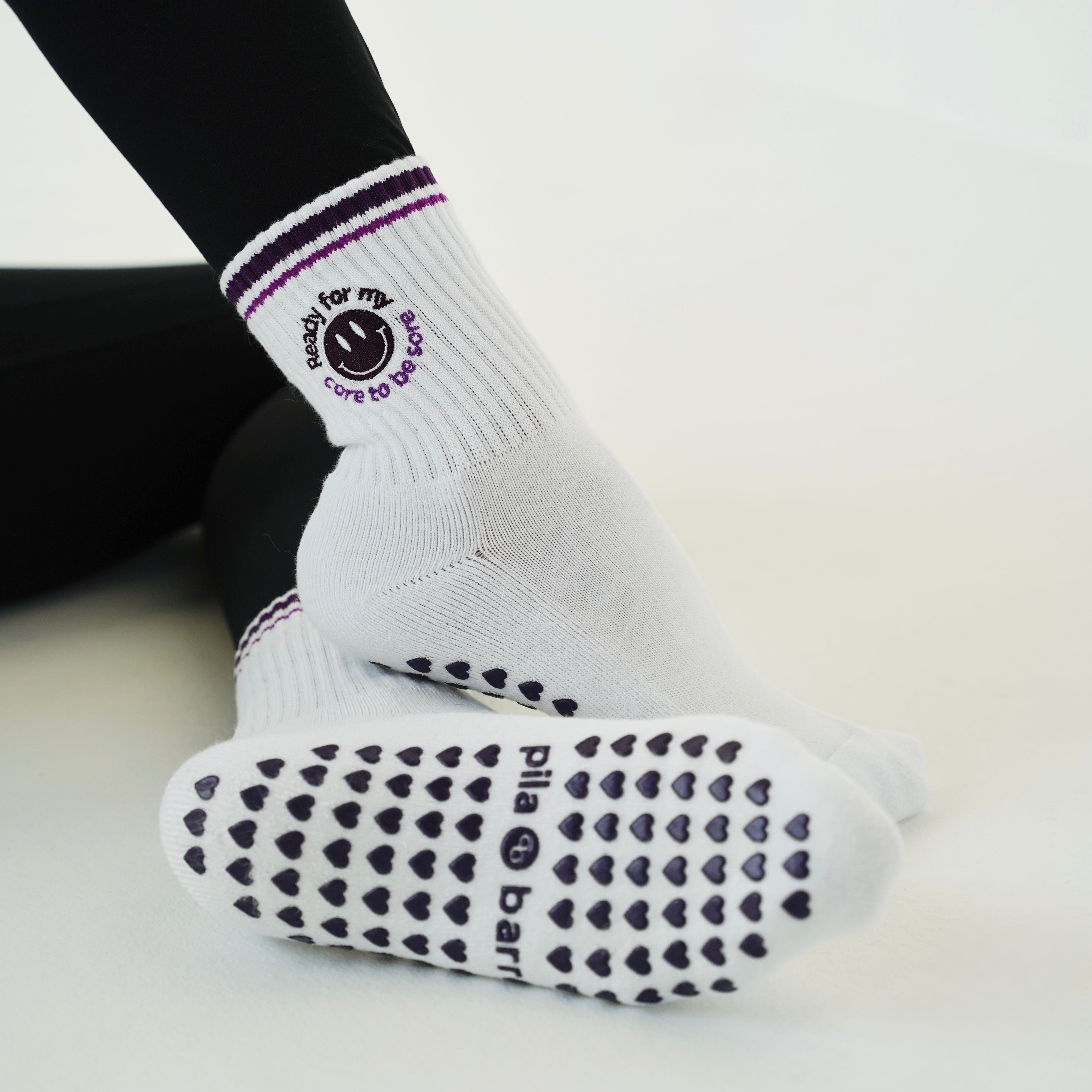 White grip socks with black heart-patterned soles and a logo on the cuff, worn with black leggings on a clean white background.