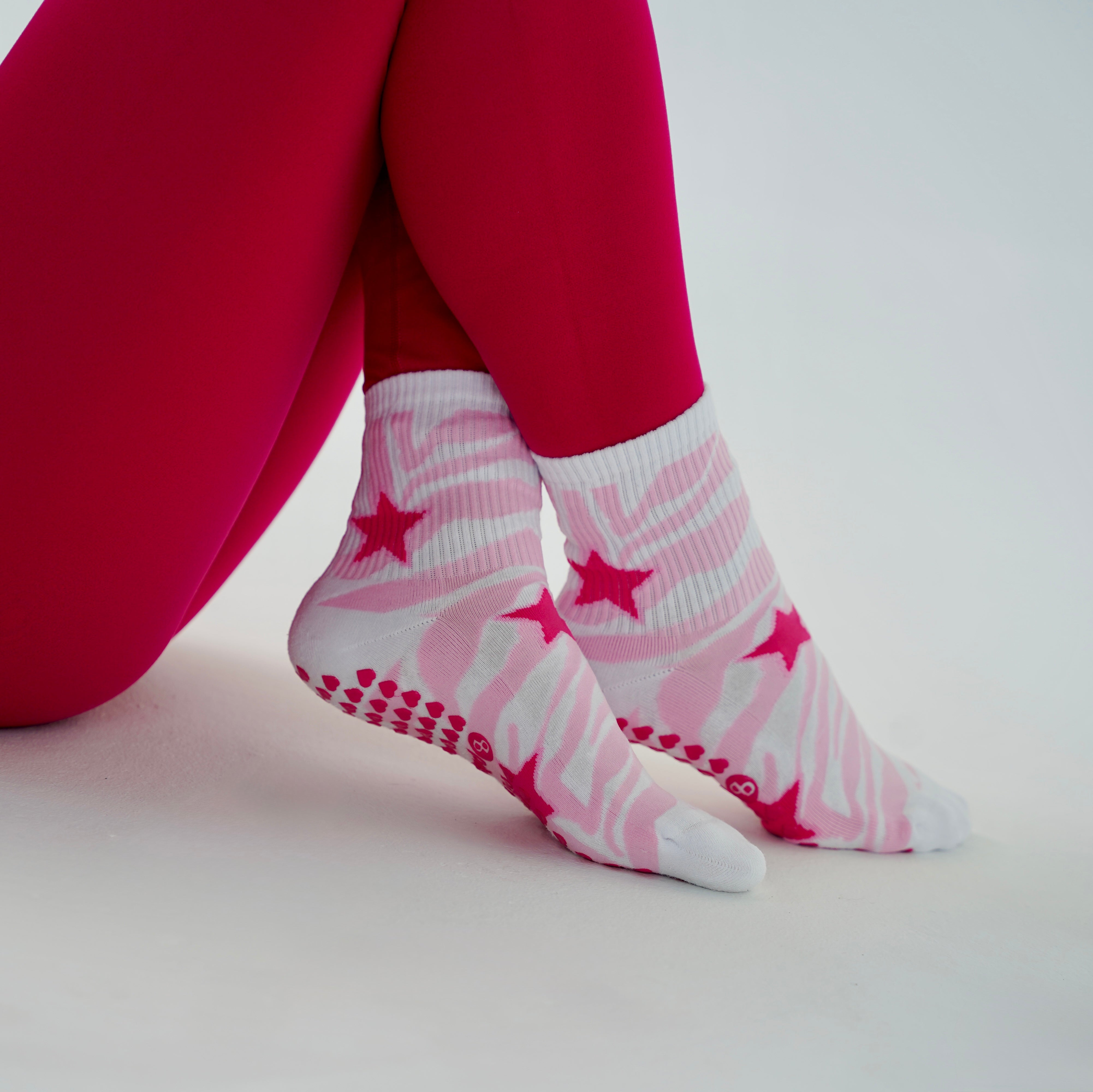White and pink zebra pilates socks with star designs, worn with bright pink leggings against a clean white background.