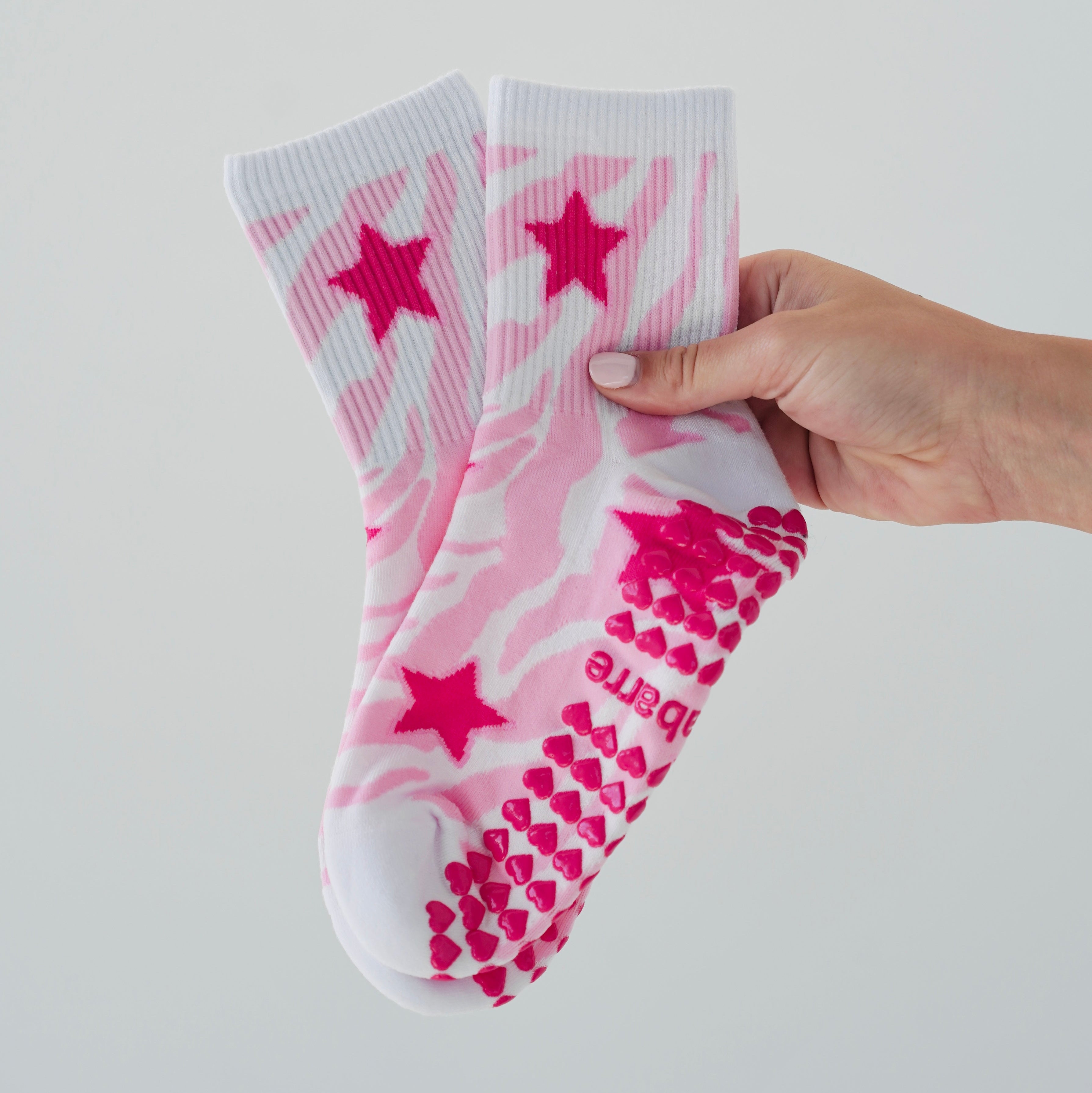 A pair of white grips socks with pink zebra stripes, pink stars, and pink grips. Cute pilates socks with zebra print