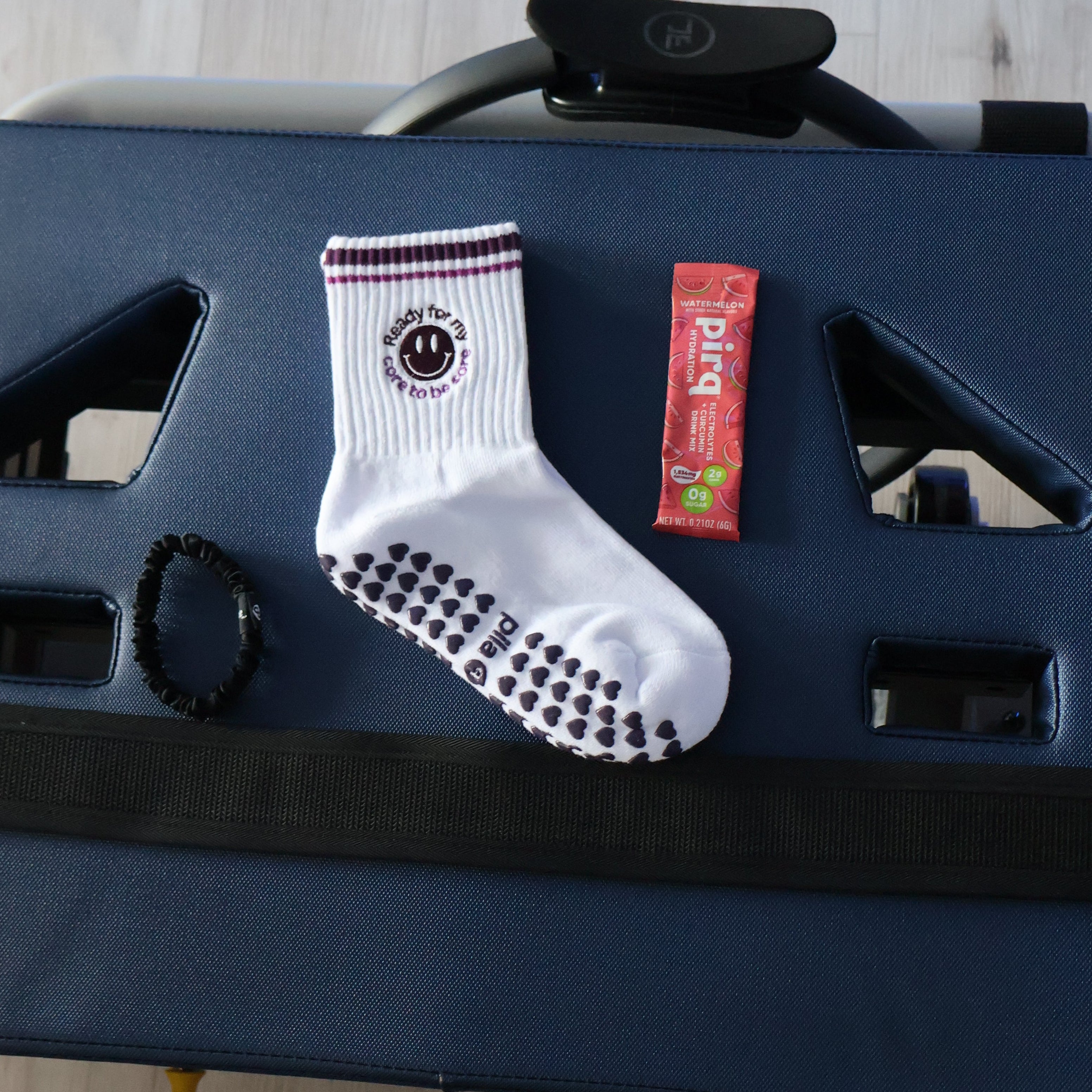 A white crew sock with purple heart grips and a smiley face, displayed on a dark blue exercise machine alongside Pirq electrolyes 
