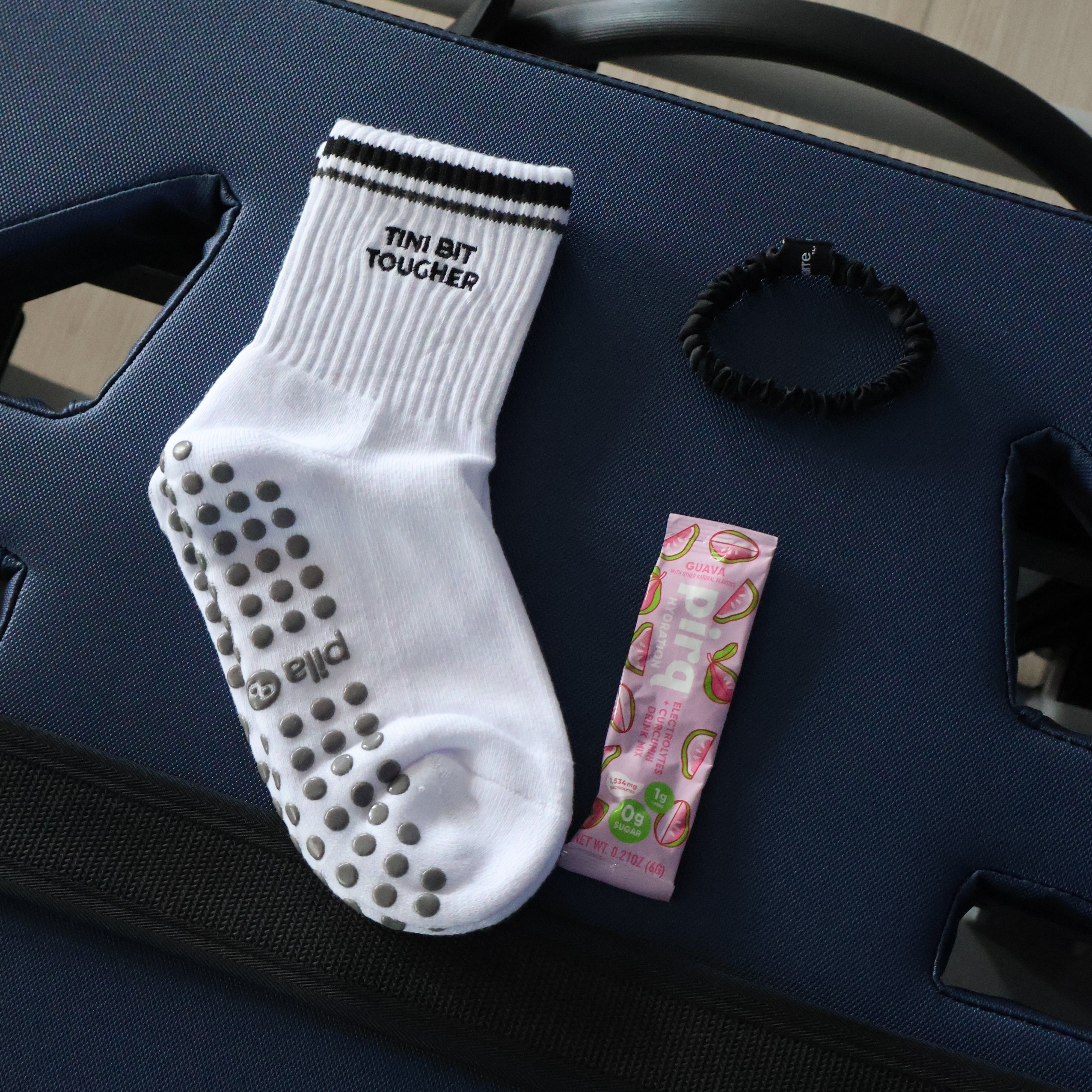 A white grip sock with black text reading 'THE BIT TOUGHER' and silver non-slip dots on the sole, displayed on a navy blue pilates refromer
